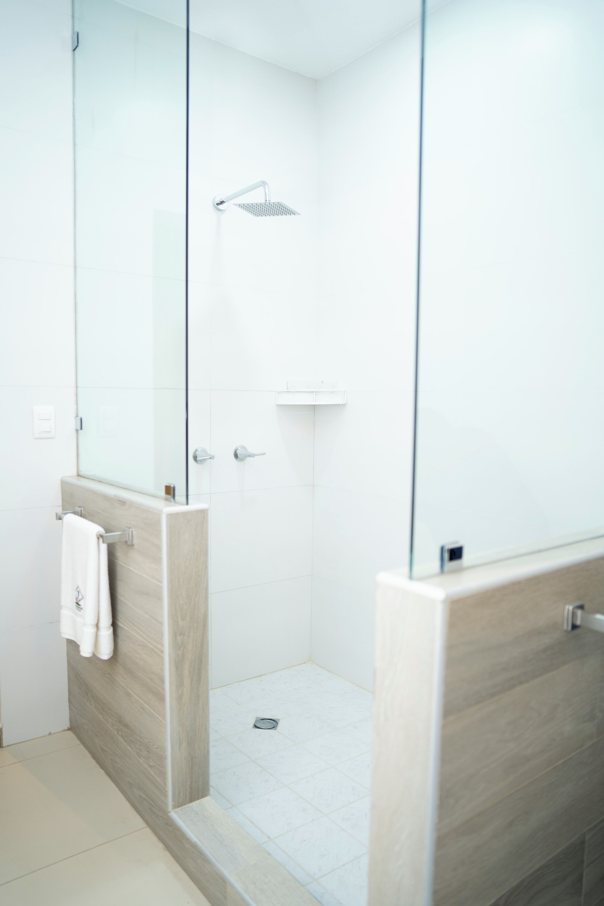 A modern bathroom with a glass shower enclosure, a white towel hanging on a rack, and a wooden vanity.