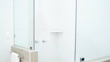 A modern bathroom with a glass shower enclosure, a white towel hanging on a rack, and a wooden vanity.