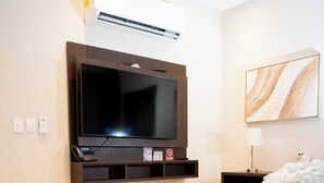Habitación de hotel con una cama grande, un televisor montado, una mesita de noche con lámpara y un equipo de aire acondicionado instalado en la pared.