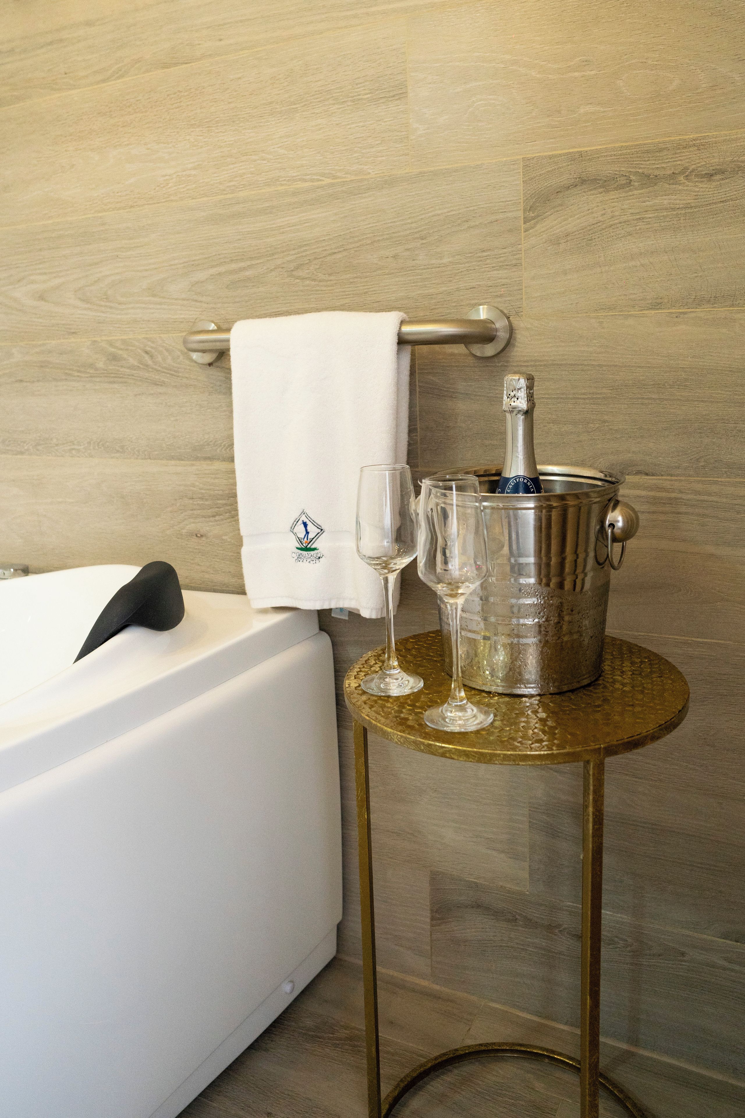 A bathroom with a bathtub, a towel, a bottle of champagne, and two glasses on a small round table.