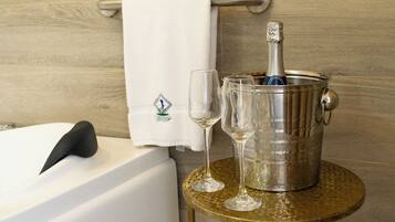 A bathroom with a bathtub, a towel, a bottle of champagne, and two glasses on a small round table.