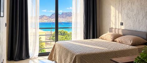 Un dormitorio con cama, mesita de noche, planta en maceta y vistas al mar y las montañas.