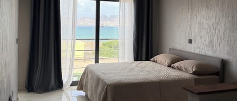 A bedroom with a bed, a nightstand, a window with curtains, and an air conditioning unit.
