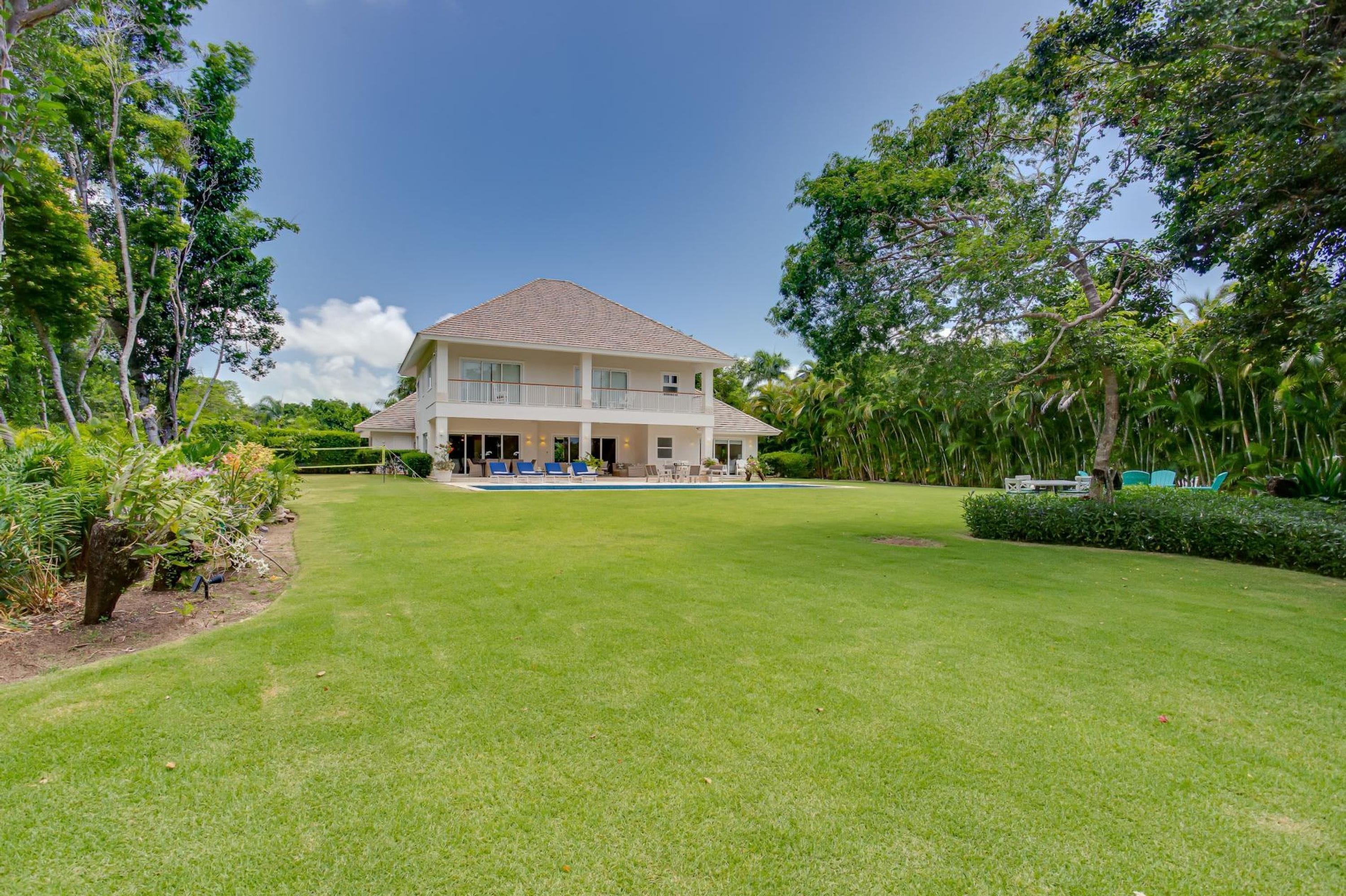 A two-story house with a swimming pool, surrounded by lush greenery and trees.