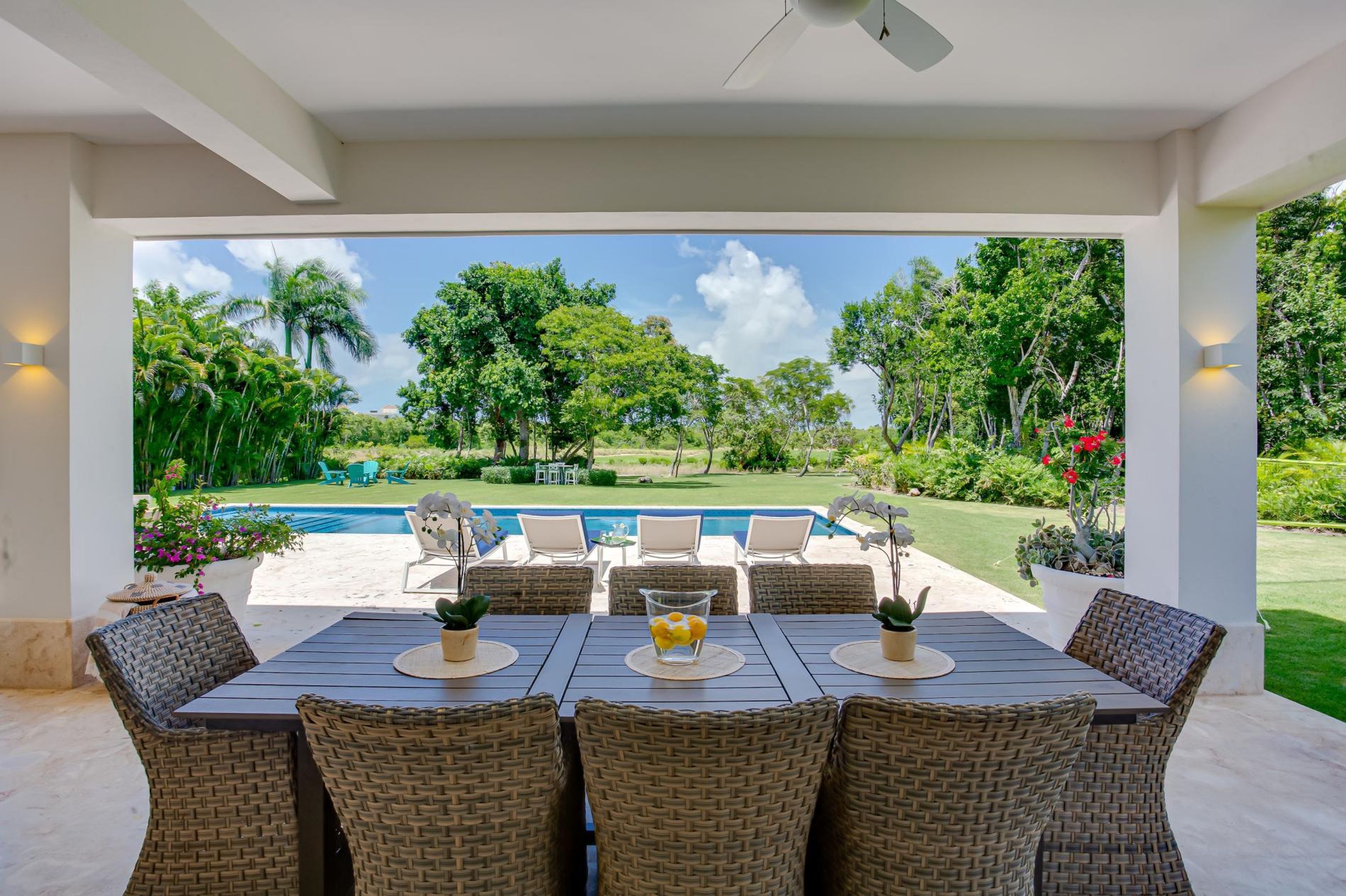 An outdoor patio with a dining table, chairs, and a view of a swimming pool and lush greenery.