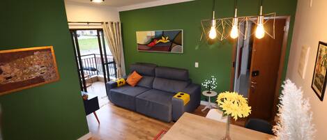 A living room with a sofa, a dining table with chairs, and a green wall with artwork.