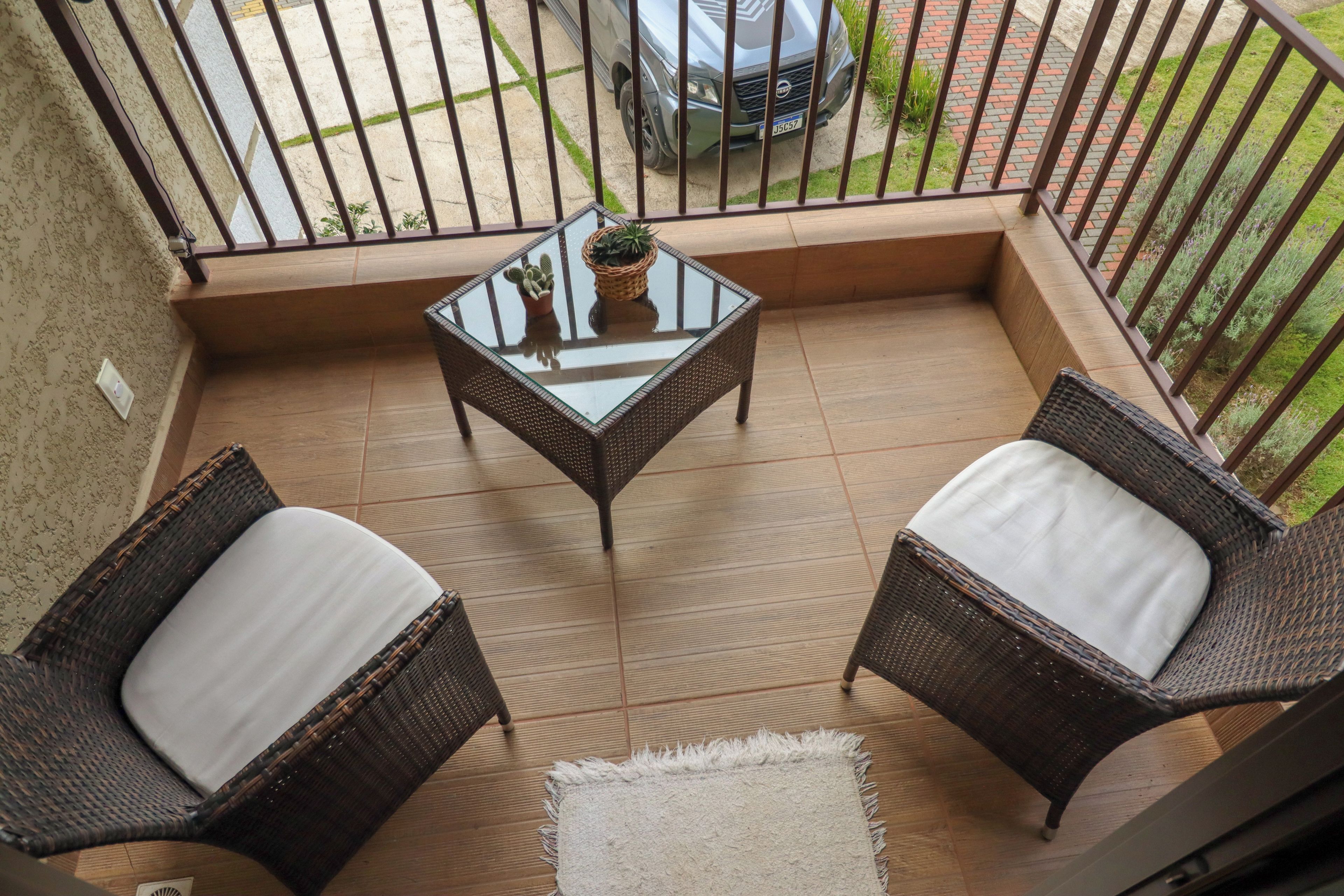 Een balkon met twee rieten stoelen, een tafel met glazen blad en een potplant.