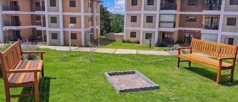 A courtyard with two wooden benches, a small fire pit, and a well-maintained lawn.
