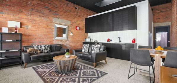 Ein stilvoller Wohnraum mit Backsteinwand, zwei Sofas, einem Couchtisch und einer Küchenzeile mit einer großen Tafel.