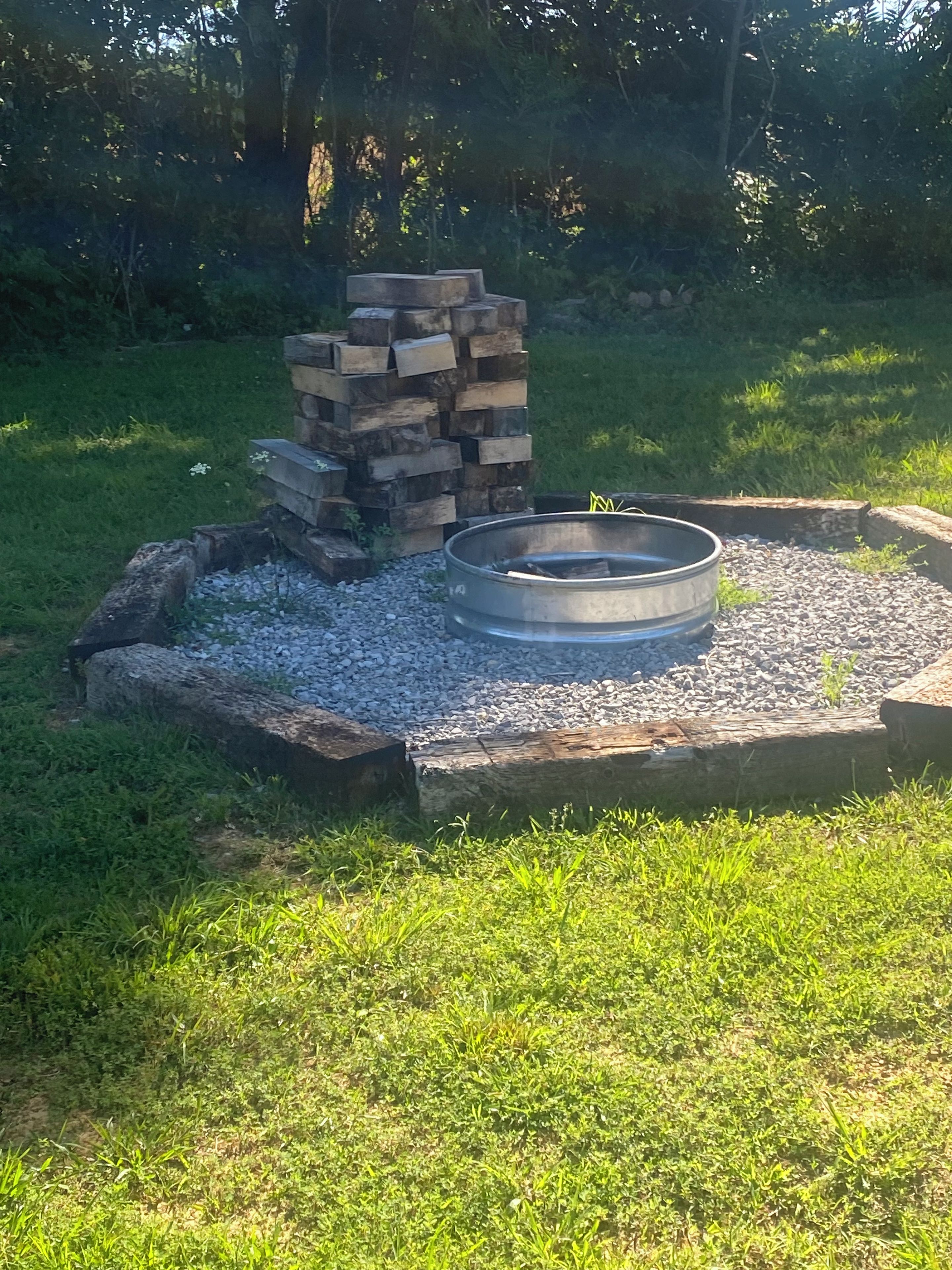 Un foyer circulaire, entouré d’une bordure en pierre, avec une pile de bois de chauffage à proximité.