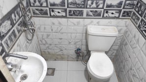 Et lille badeværelse med en hvid vask, toilet og brusebad. Væggene er fliset med et mønster af sort-hvide billeder.