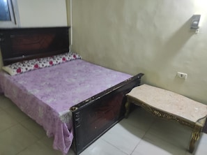 Una habitación con una cama, un banco y una lámpara fijada en la pared.