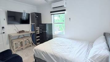 Une chambre à coucher comprenant un lit, un bureau, une chaise, un téléviseur et un appareil de climatisation.