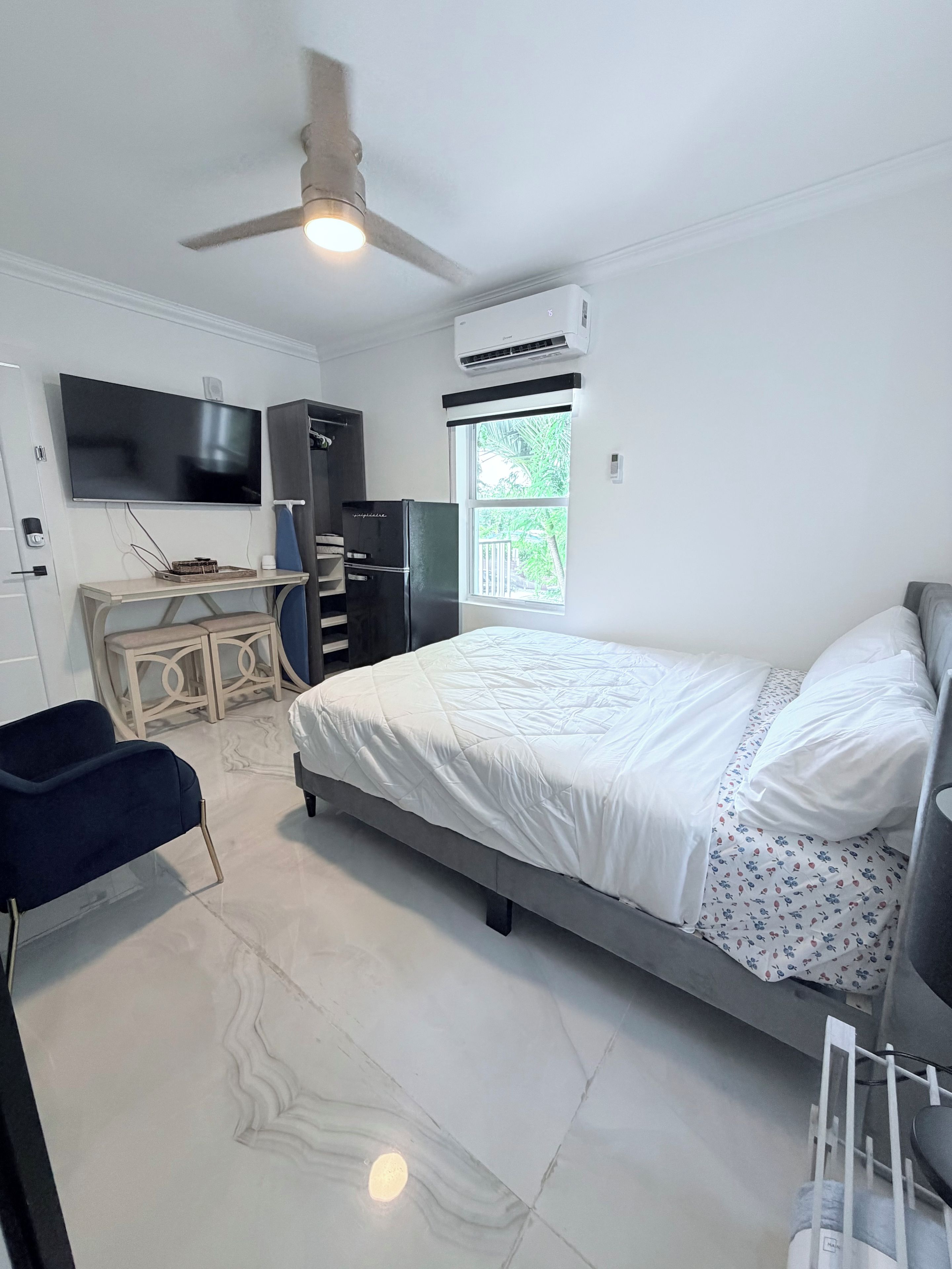 A modern bedroom with a bed, a desk, a chair, a ceiling fan, and a window.