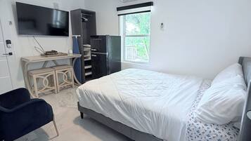 A modern bedroom with a bed, a desk, a chair, a ceiling fan, and a window.