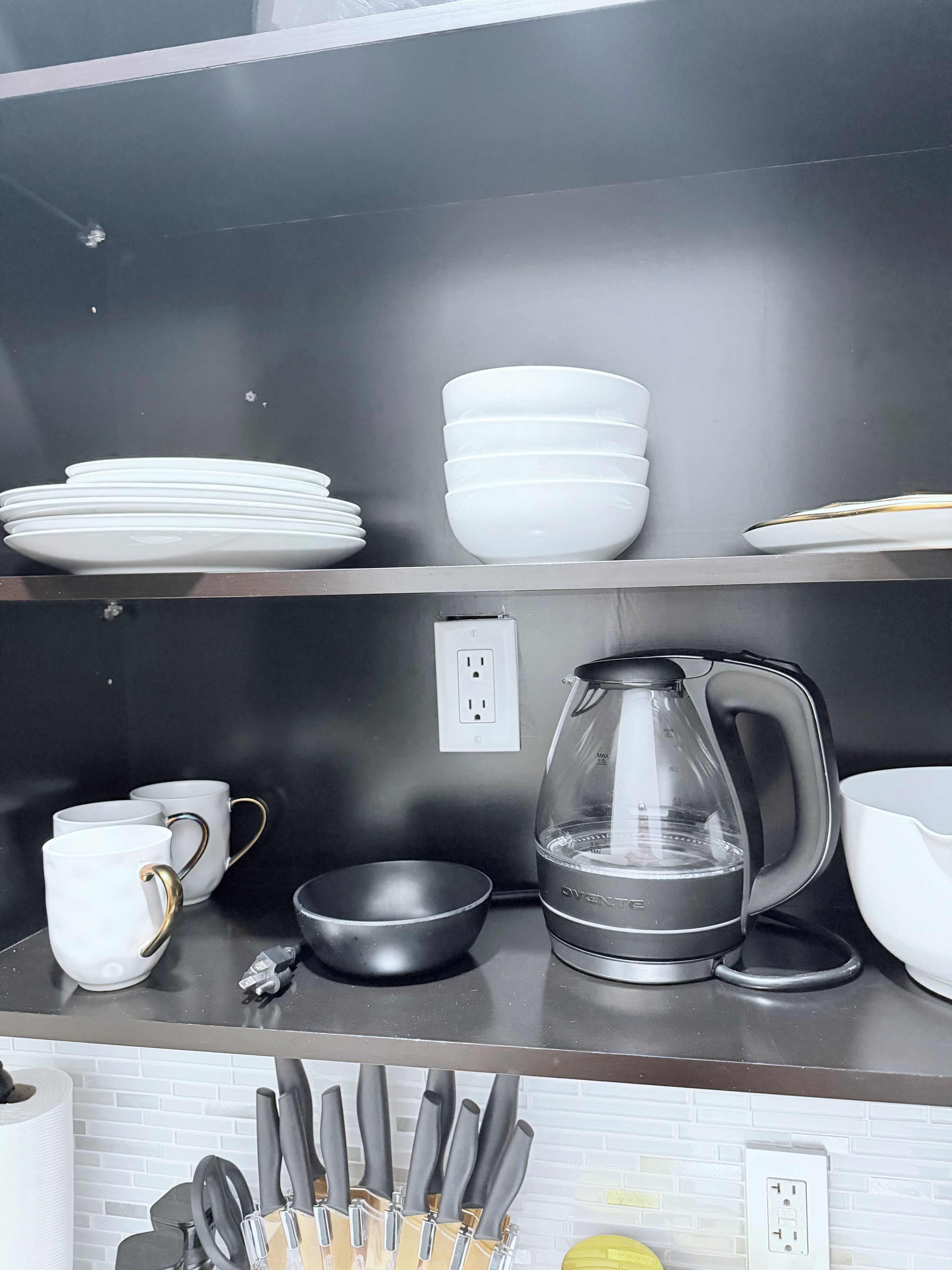 A kitchen counter with white plates, bowls, a coffee maker, and a knife block.