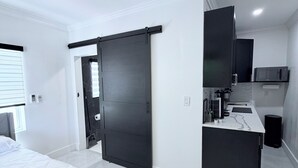 A modern bedroom with a bed, a ceiling fan, and a sliding door leading to a kitchen area. - Cozy studio apartment in tranquil Tavernier with AC and kitchen. (Tavernier)