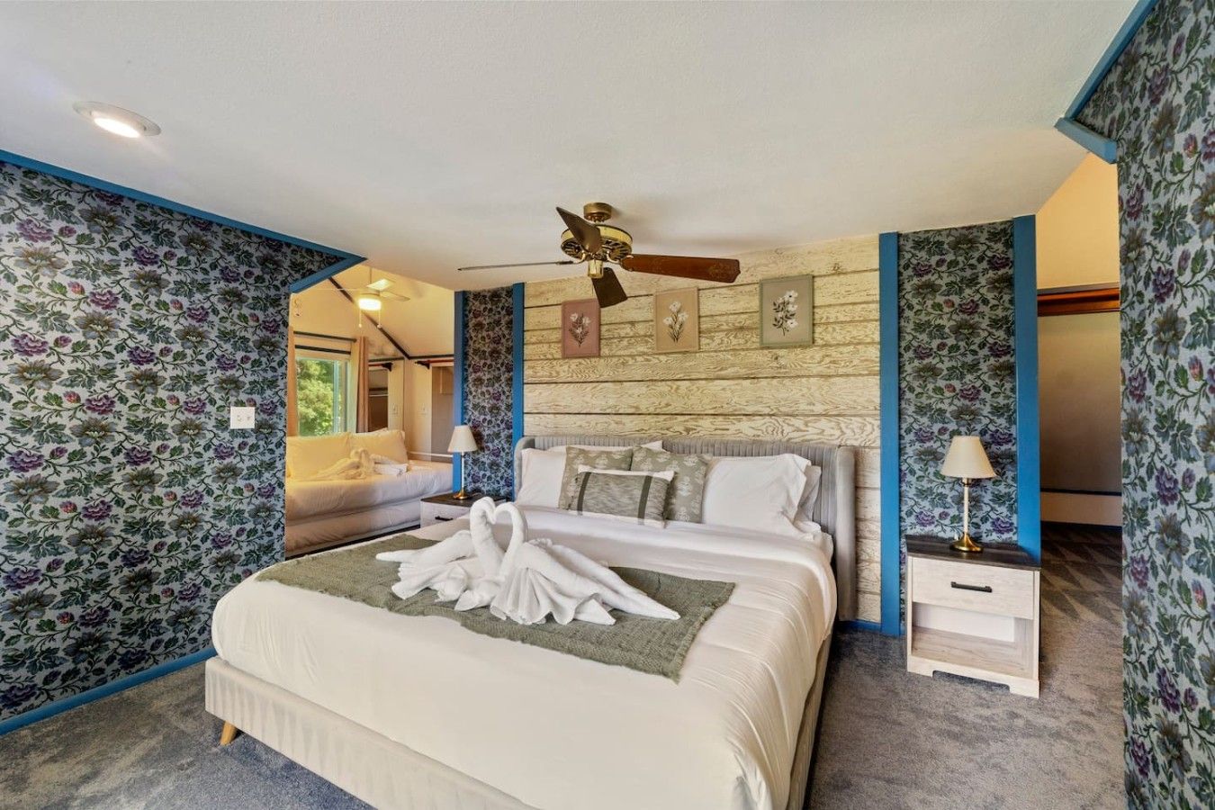 Habitación de hotel con una cama grande, ventilador de techo y papel tapiz floral.