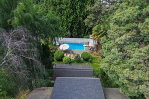 A residential property with a swimming pool, surrounded by dense greenery and trees. - Storybook Upper Suite | Pool, Hot Tub, BBQ Grill (Seattle)