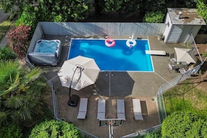 A backyard with a swimming pool, lounge chairs, a hot tub, and a covered patio area.