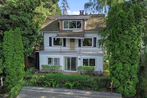 A two-story house with a balcony, surrounded by dense greenery.