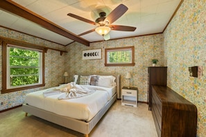 A bedroom with a bed, a ceiling fan, a nightstand, a dresser, and floral wallpaper.
