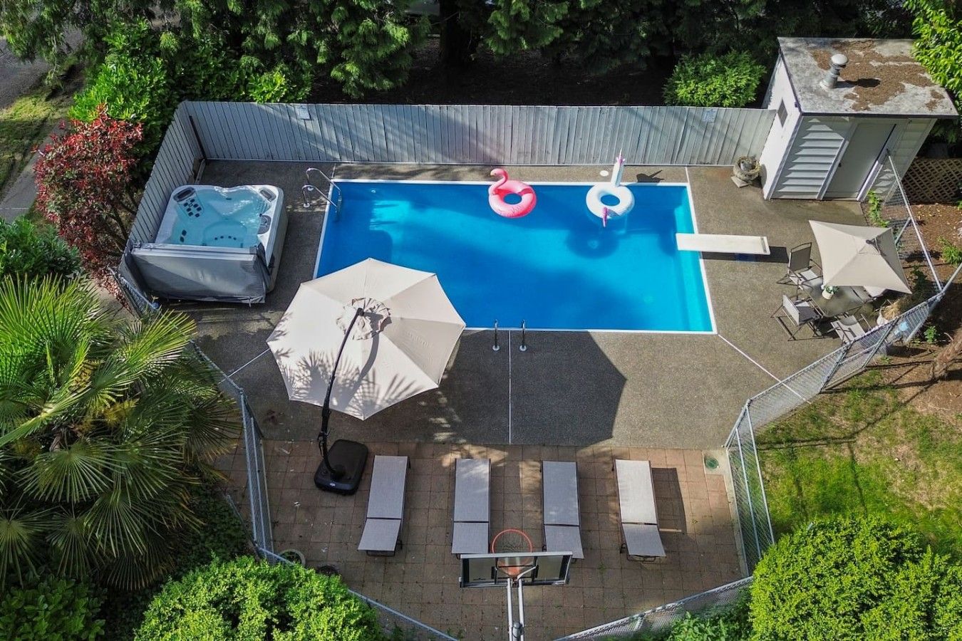 Een achtertuin met een zwembad, lounge stoelen, een jacuzzi en een overdekt terras.