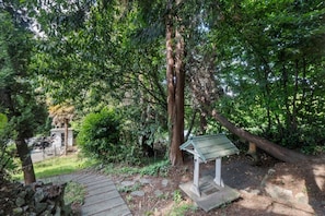 A stone pathway leading to a small gazebo in a wooded area with trees and a stone wall.