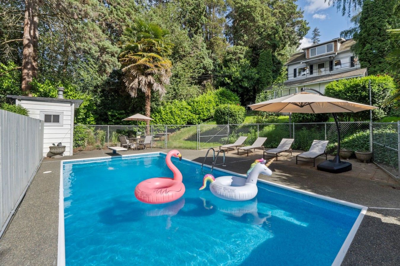Piscina com dois cisnes infláveis, rodeada por um espaço de estar cercado, com espreguiçadeiras e guarda-sóis.