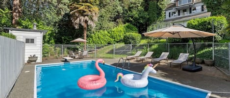 Une piscine agrémentée de deux cygnes gonflables, entourée d’une terrasse délimitée par une clôture, avec des chaises longues et des parasols.
