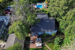 An aerial view of a residential area with a house, a swimming pool, and surrounding greenery.
