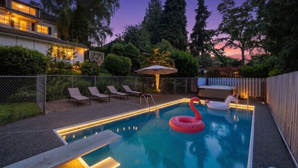 A swimming pool with lounge chairs and a flamingo float, surrounded by a fence and trees. - Cozy Garden Suite w/ Pool & Hot Tub | Near Airport (Seattle)