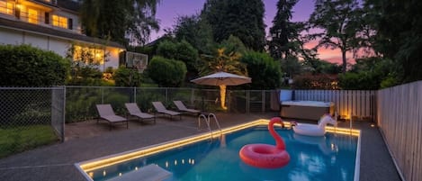 A backyard with a swimming pool, lounge chairs, and a flamingo float.