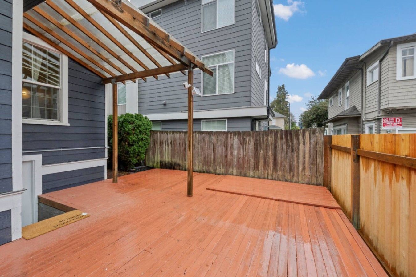 Un terrazzo in legno con una pergola, una recinzione di legno e una casa sullo sfondo.