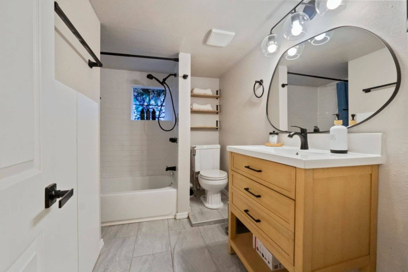 A bathroom with a bathtub, toilet, vanity with drawers, and a large mirror with lights.