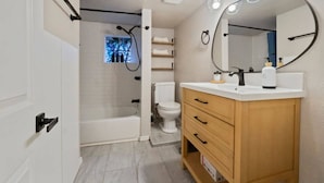 Ein modernes Badezimmer mit Badewanne, Toilette, Waschtisch mit Schubladen und einem großen, beleuchteten Spiegel.