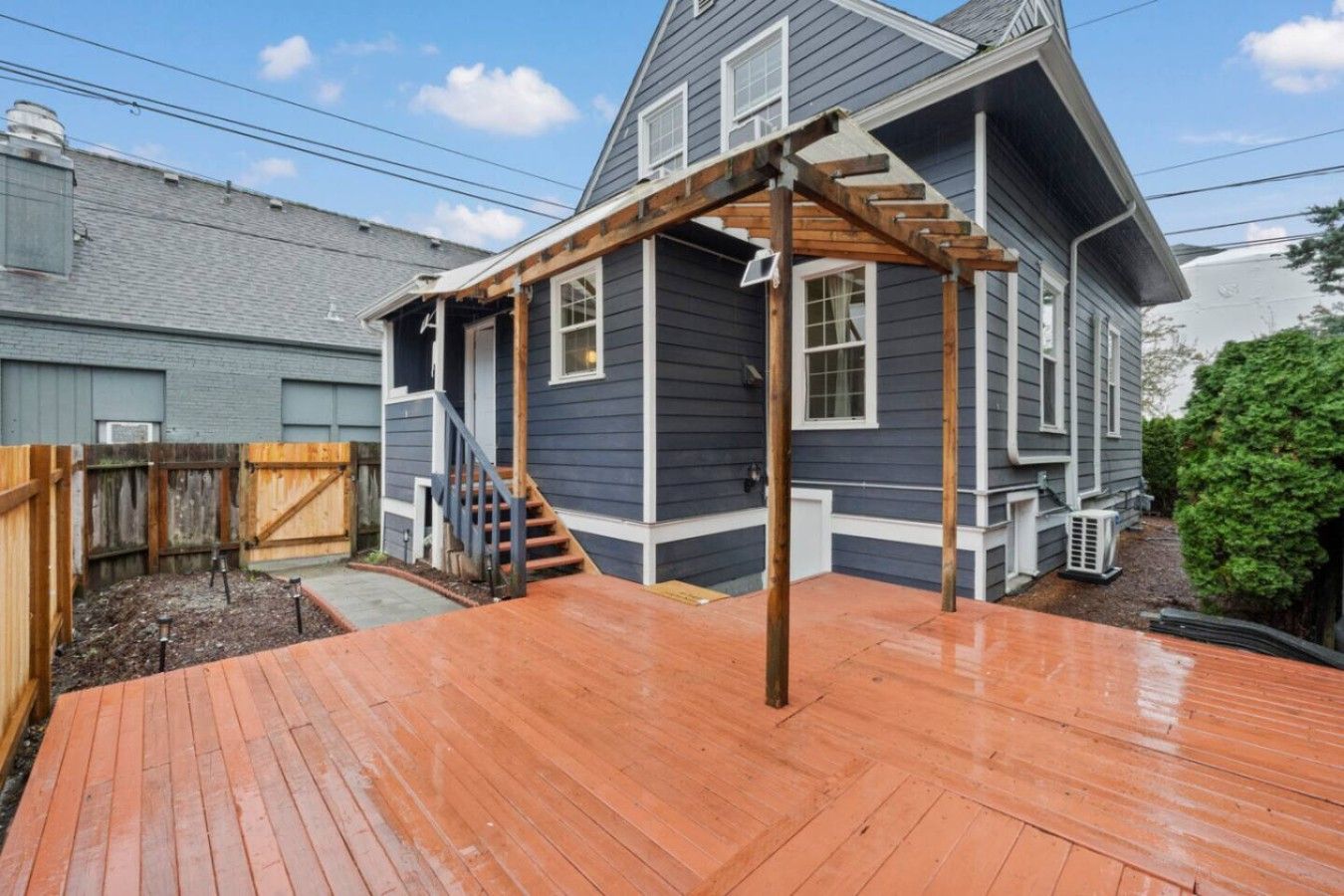A residential deck with a wooden pergola, a staircase leading to a garage, and a fenced backyard.