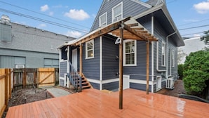 Eine Wohnterrasse mit einer Holztreppe, die zu einem Haus mit dunkel gefärbter Außenverkleidung führt.