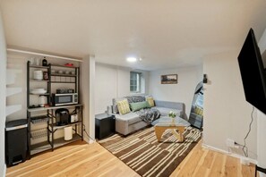 A compact living space with a sofa, coffee table, and a kitchenette area with a microwave and coffee maker. - Cozy 1BR/1BA Lower Unit Near UW | Walk to Campus (Seattle)