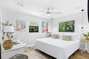 A bedroom with a bed, a ceiling fan, artwork on the walls, and a window with blinds. - Southbound Haven (Cape Coral)