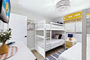 Uma cama de beliche infantil com acabamento branco, uma mesa de cabeceira com abajur e uma prateleira na parede com uma fotografia.
