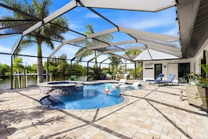 A pool area with a hot tub, lounge chairs, and a covered patio. - Southbound Haven (Cape Coral)