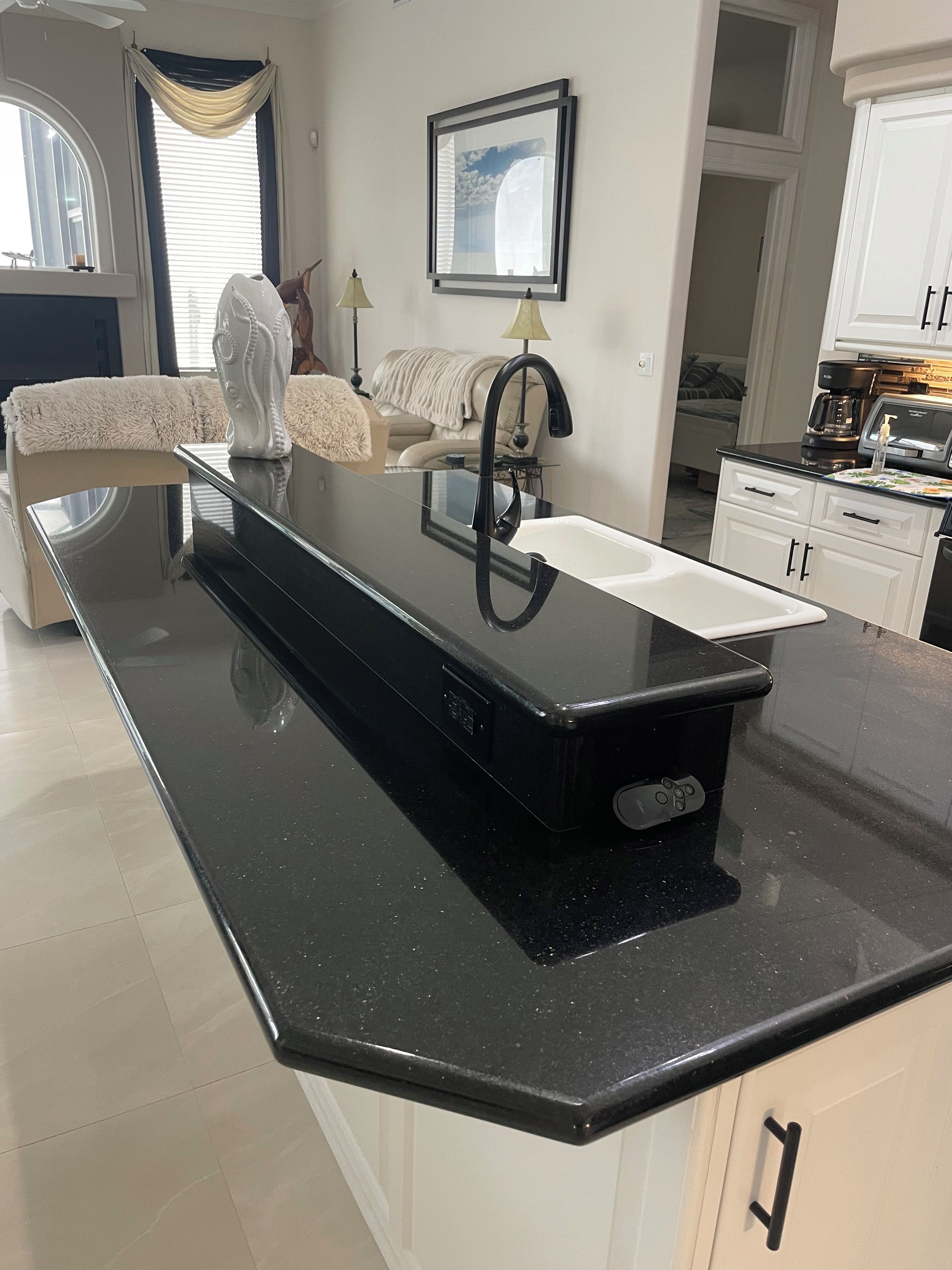 Una cucina con un piano di lavoro nero, mobili bianchi, una macchina da caffè e un quadro appeso al muro.