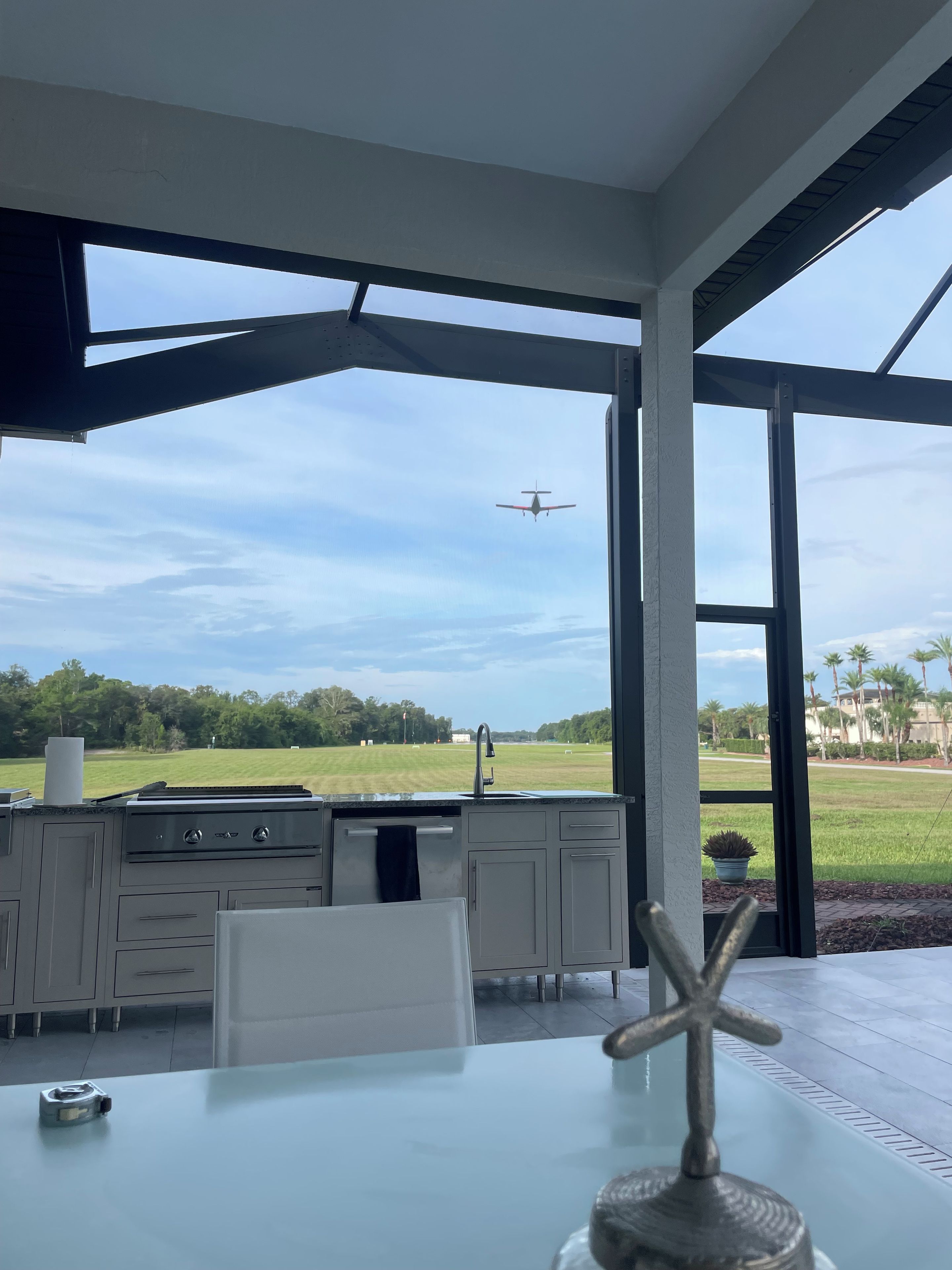 A modern kitchen with a large window overlooking a grassy field and a clear sky.