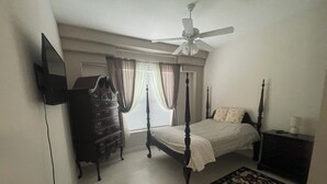 Un dormitorio con una cama con dosel, un tocador, un ventilador de techo y una ventana con cortinas.
