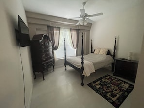 Quarto com cama de dossel, penteadeira, ventoinha no teto e janela com cortinas.