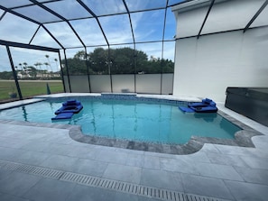 Piscina com cobertura de vidro, rodeada por um deck pavimentado e um edifício branco.