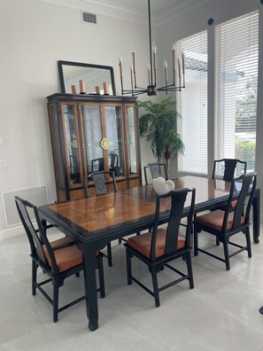 Uma sala de jantar com uma mesa de madeira grande, seis cadeiras, um armário de madeira escura e um vaso com planta.