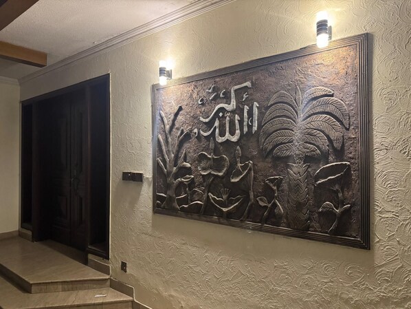 A hallway with a textured wall and a large decorative panel with Arabic calligraphy.