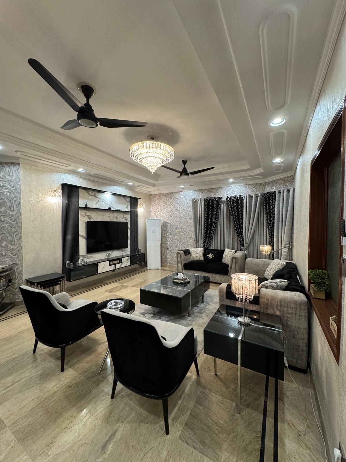 Un salon moderne doté d’un téléviseur à écran plat, d’un ventilateur de plafond et d’un lustre.